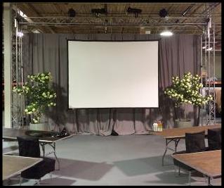 wharehouse turnned into a meeting room with pipe and drape as well as large projection screen and stge lighting